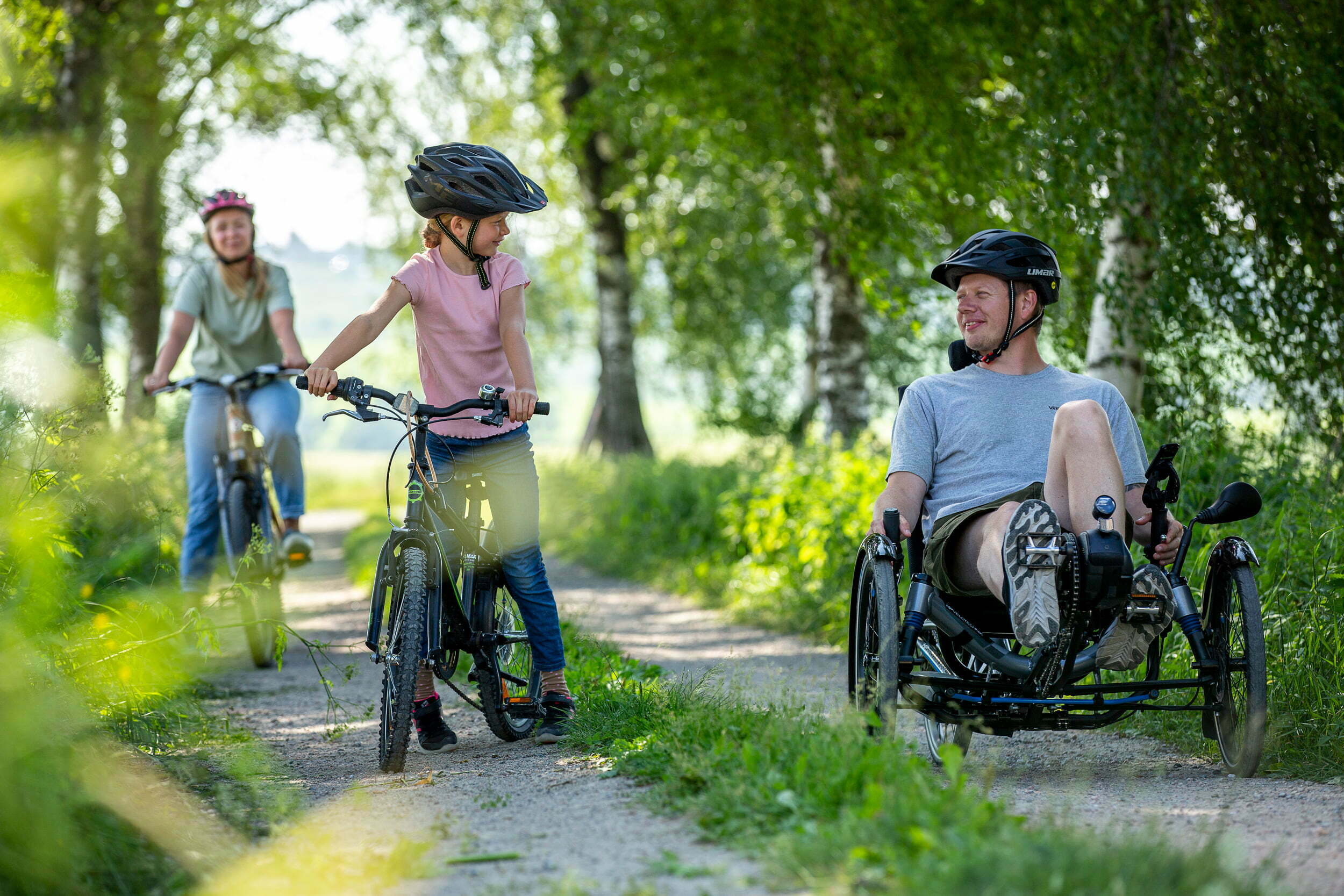 En familie på sykkeltur i skogen. Mamma, datter og pappa. Pappaen sykler på en sittesykkel.