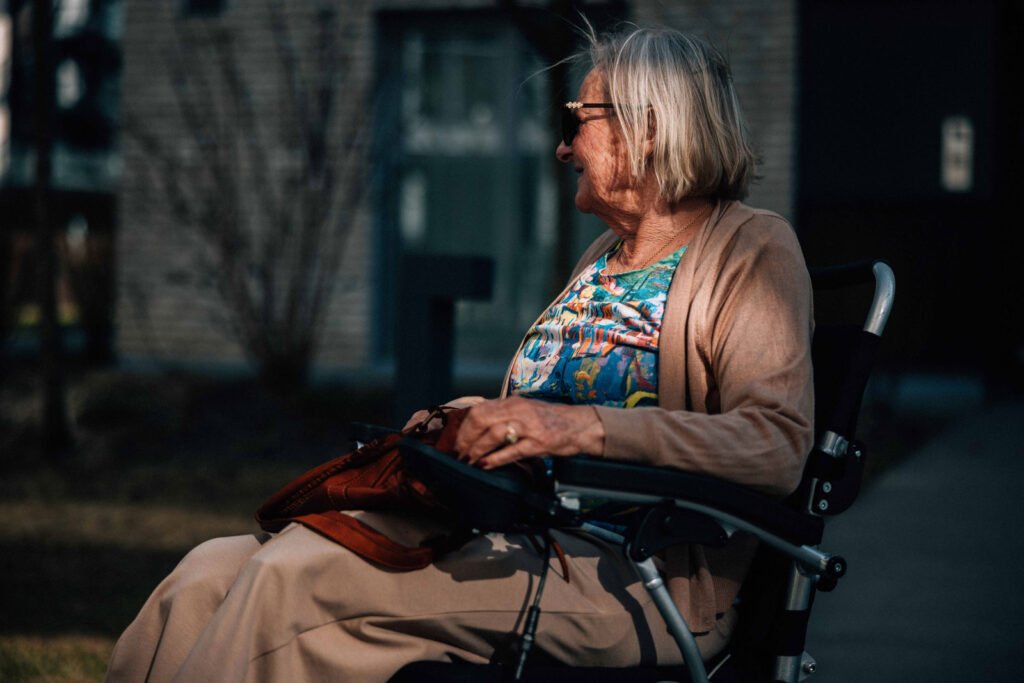 Nærbilde av Synnøve. Hun sitter i en elektrisk rullestol med vesken sin i fanget. Bildet er tatt fra siden og hun ser fremover.