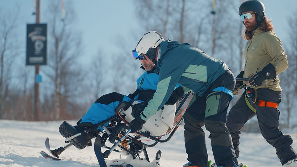 En instruktør hjelper en som skal kjøre sitski med å forklare hvordan han skal benytte krykkeskia under kjøring.