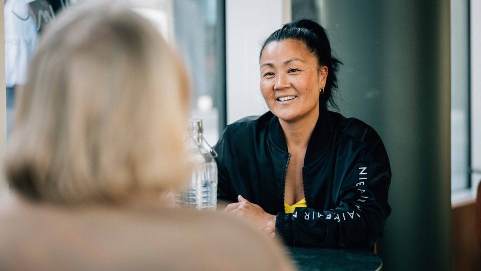 Beate ser på Synnøve. Vi ser bakhodet til Synnøve og Beate forfra.