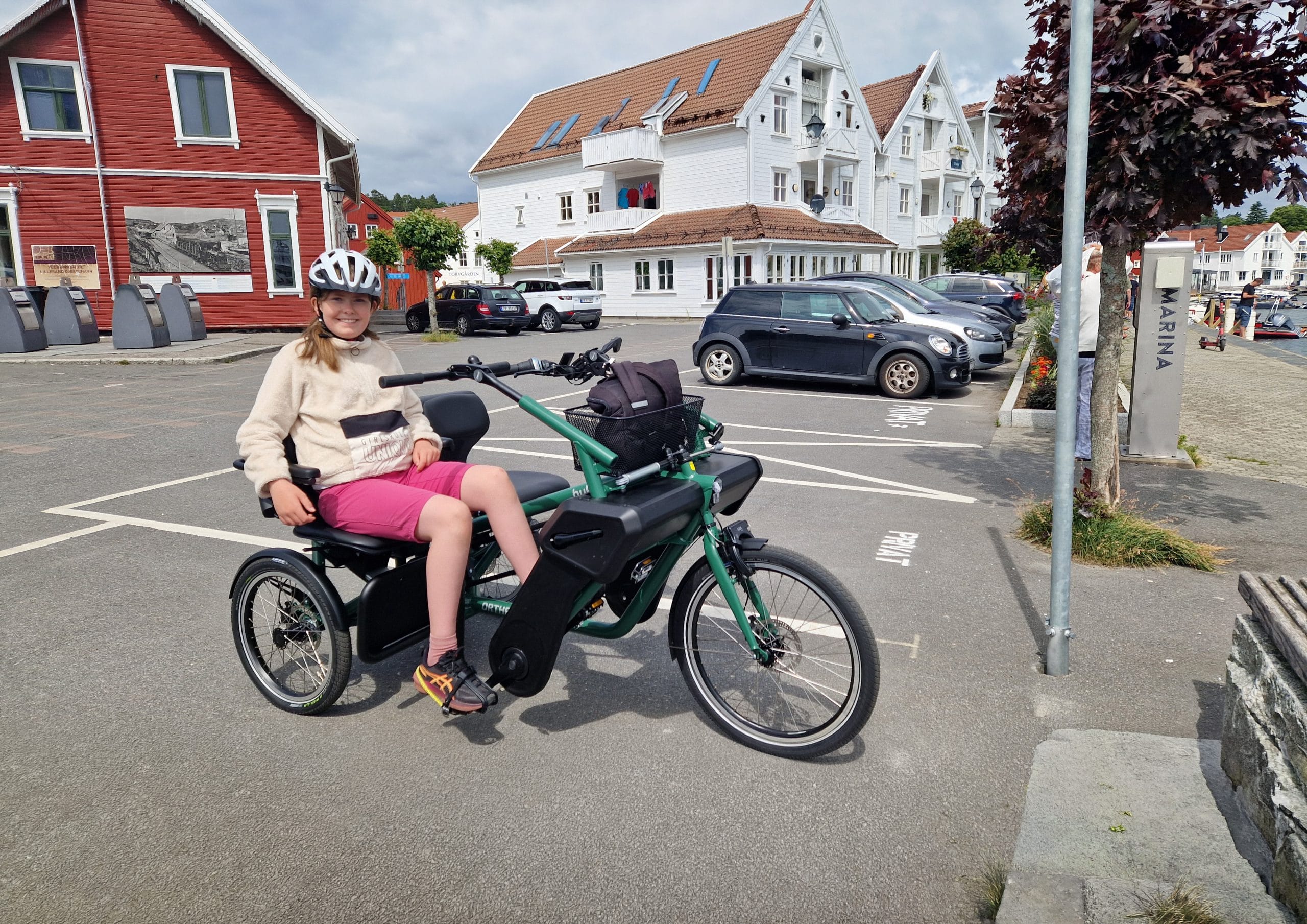 En jente på 11 år sitter på Orthros tandemsykkel på en parkeringsplass på sørlandet. Hun har på hjel, lys genser og shorts.