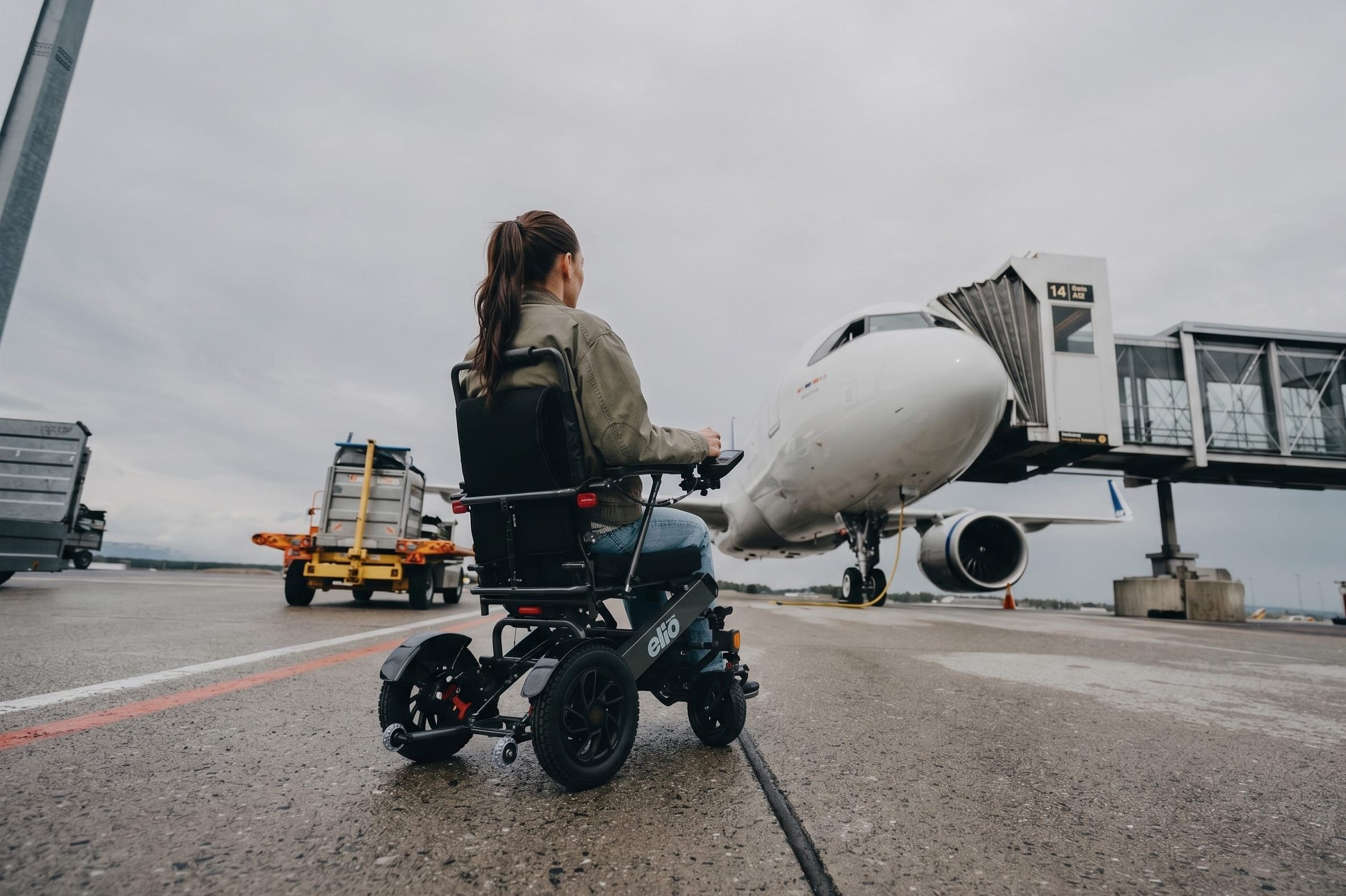 En dame ser mot flyet ute på rullebanen. Du ser henne bakfra, sittende i elio sammenelggbare elektriske rullestol.
