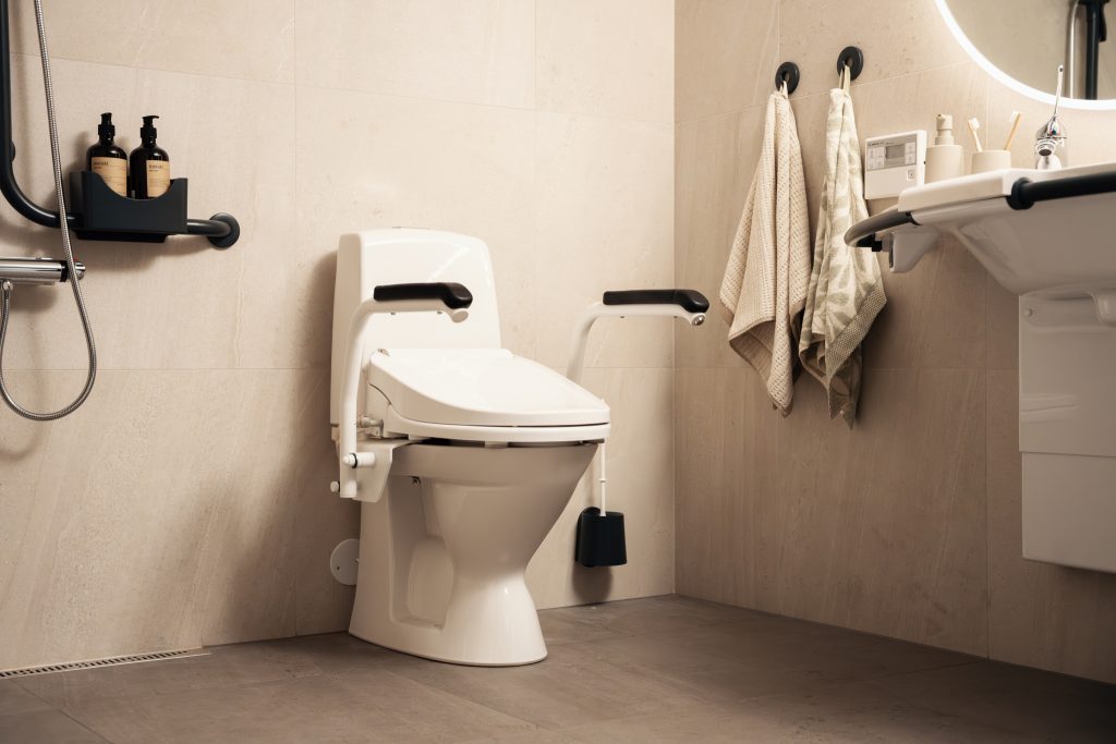 Bano Clean 700 spyl- og tørkesete med armlener montert på et vanlig guvlstående toalett på et moderne bad.
