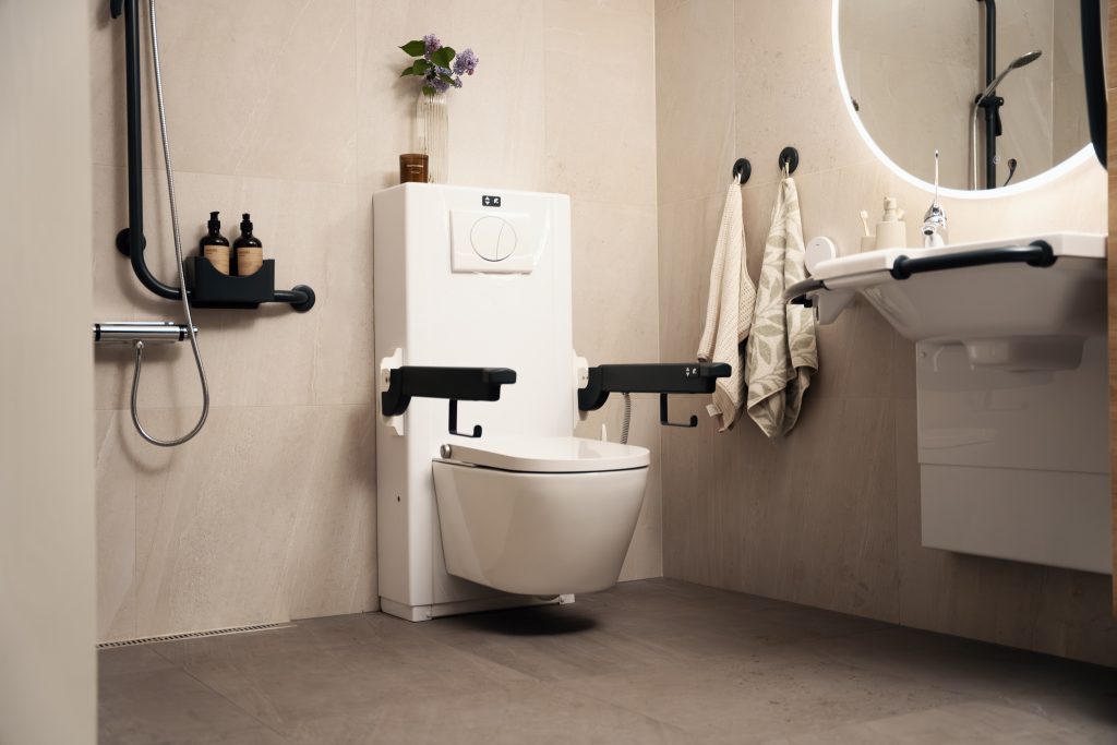 Bano Clean Comfort vegghengt toalett med Bano elektrisk sisterne i et moderne pent bad. Vasken og toalettet har armlener og støttehåndtak.