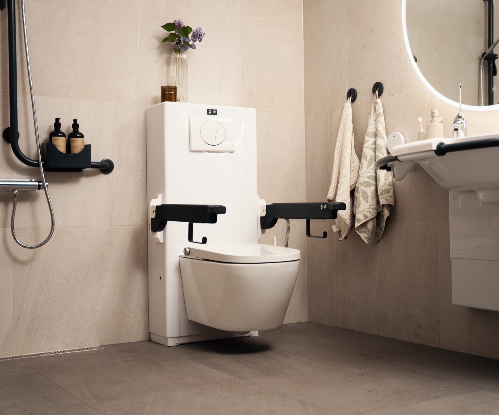 Bano Clean Comfort vegghengt toalett med Bano elektrisk sisterne i et moderne pent bad. Vasken og toalettet har armlener og støttehåndtak.